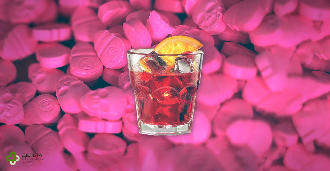 Розовые таблетки экстази на фоне бокала с алкоголем